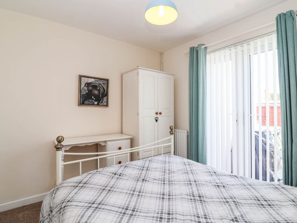 A bedroom with a bed, desk, wardrobe, and curtains at 56 Steart Gardens in Burnham-on-Sea