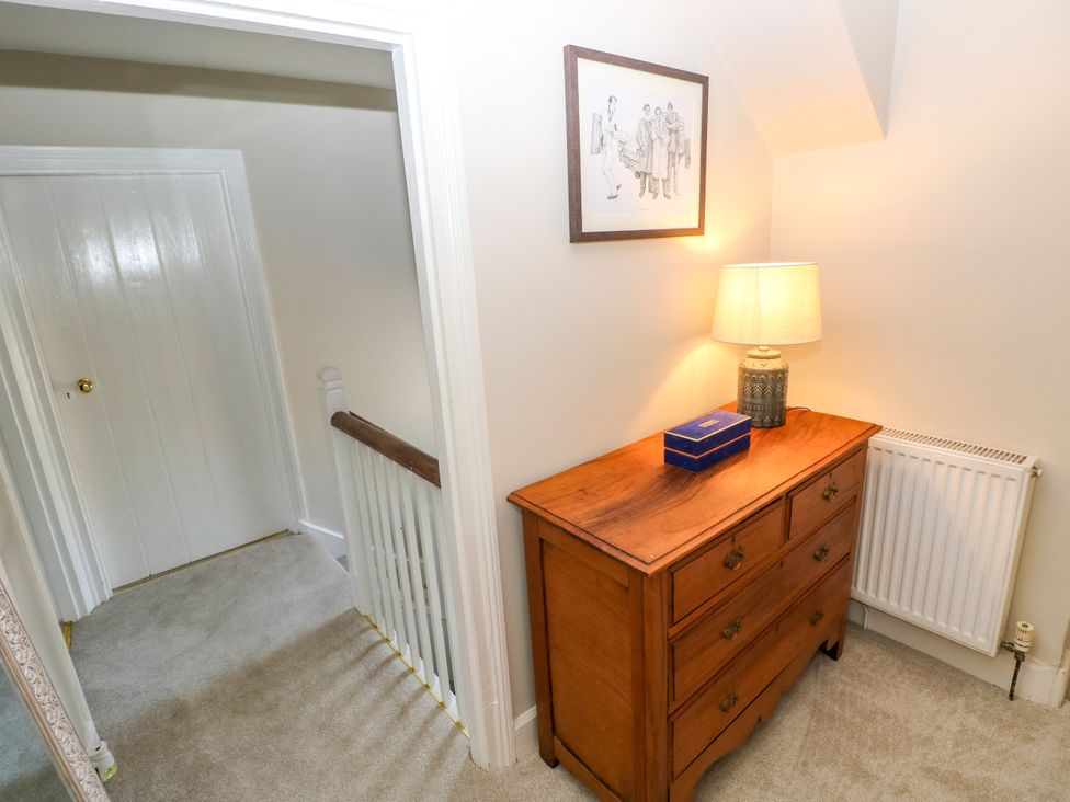 A hallway with a dresser, lamp, and framed artwork at St.Twynells Farm in Pembroke