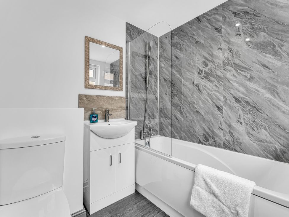 A bathroom with a toilet, sink, bathtub, and mirror at Victoria House, Stoke on Trent