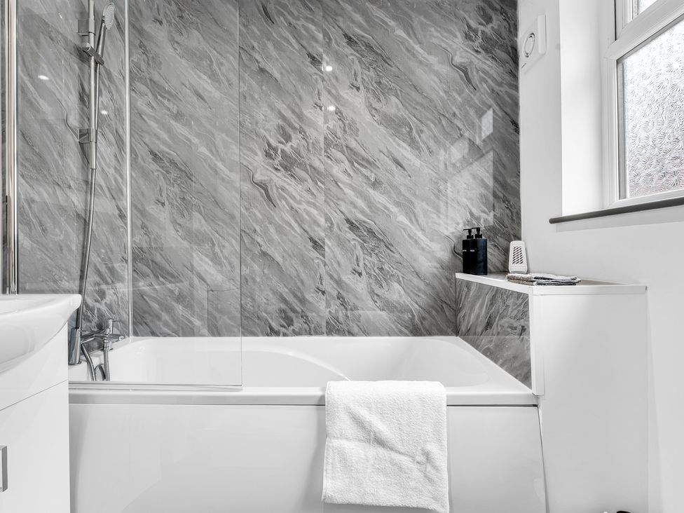 A bathtub and shower area with a gray wall at Victoria House, Stoke on Trent