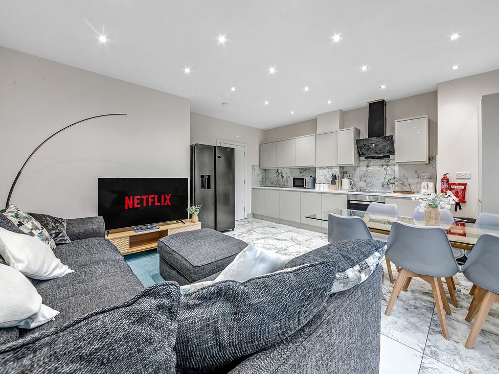 A living room with a sofa, television, and kitchen area at Oxford City Stay – Cowley House in Oxford