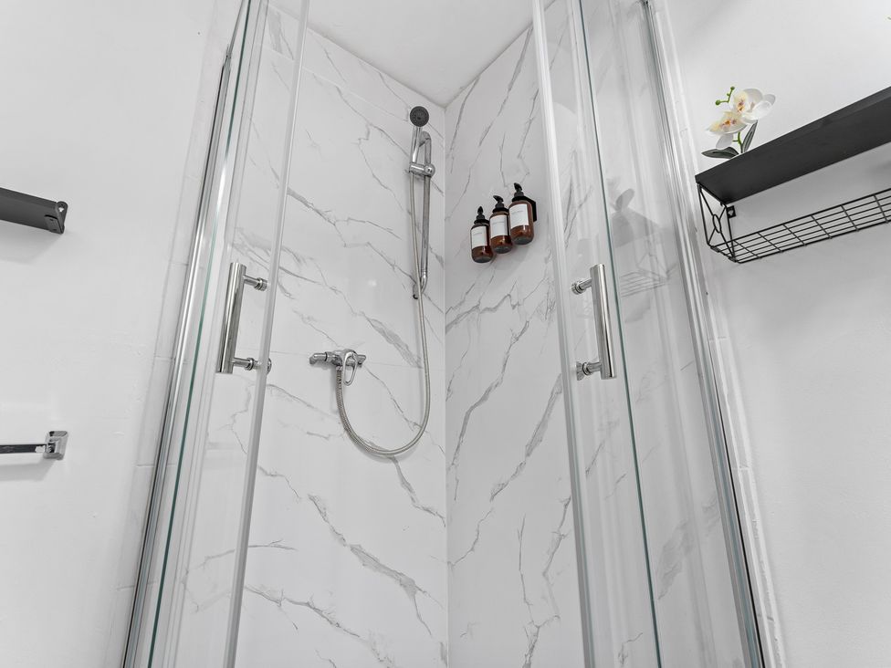 A shower with glass doors and bath products on a shelf at The Craftsman Birmingham City Apartment Birmingham
