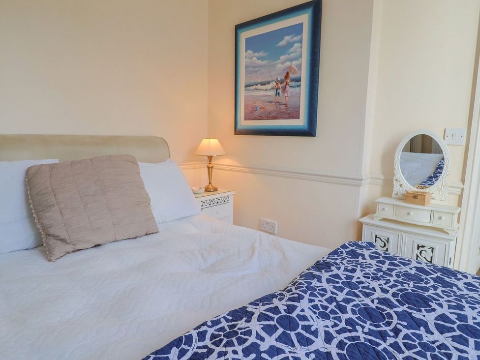 A bedroom with a bed, nightstand, lamp, and framed picture at 2 St. Michaels House in Lyme Regis