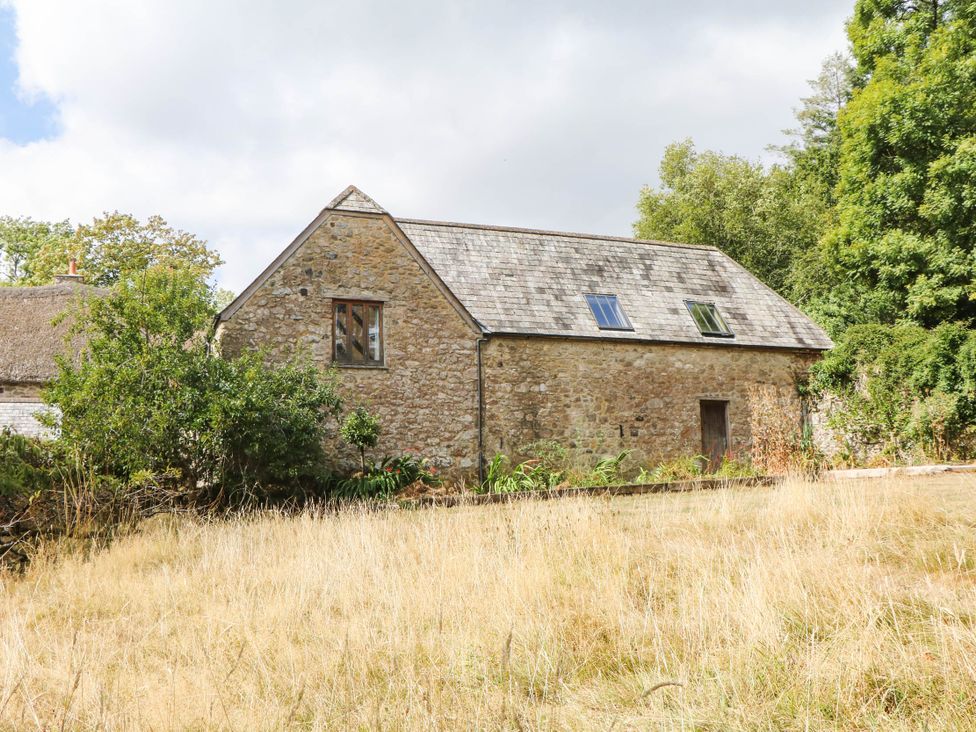 A stone house with a pitched roof and windows surrounded by grass at The Hayloft at Manaton