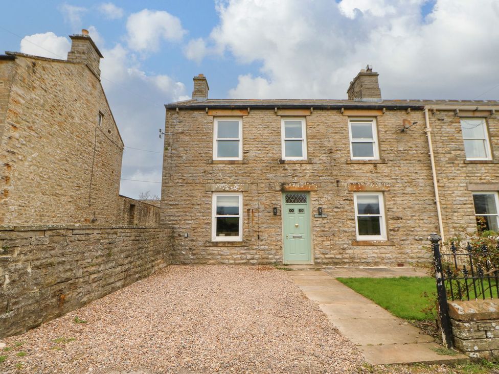 An exterior view of a stone house with a gravel driveway at Hillside House in Leyburn