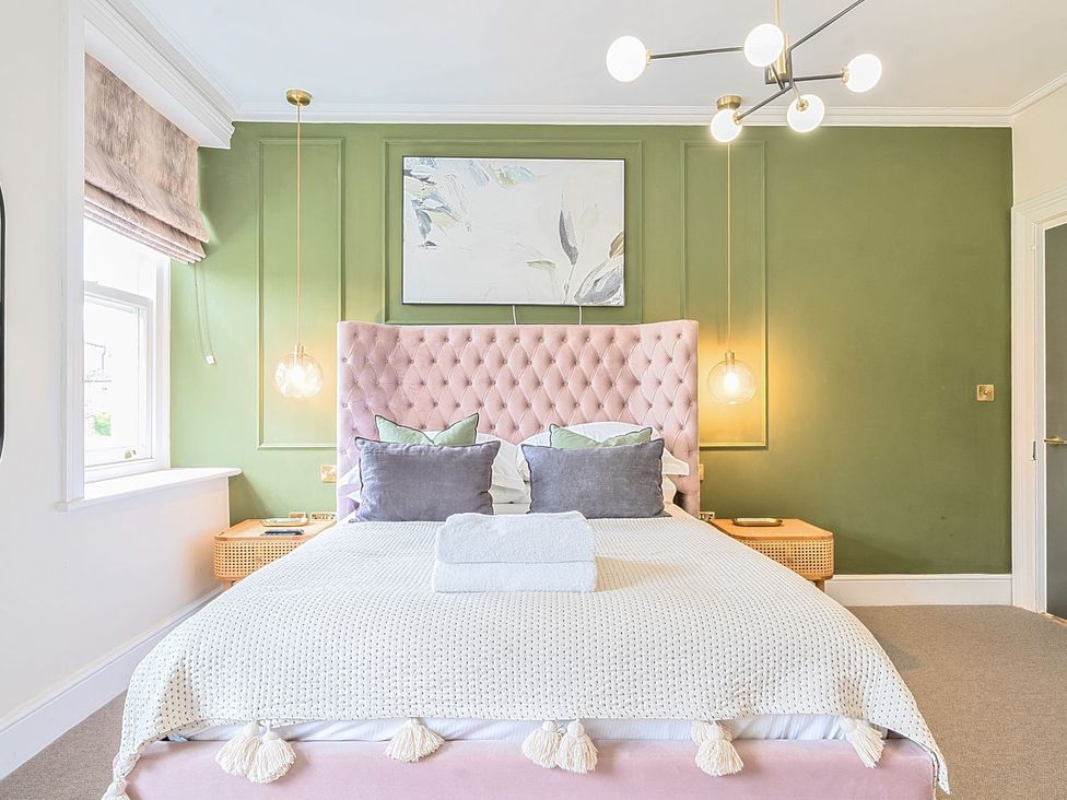 A bedroom with a pink headboard and artwork at Hillside House Leyburn