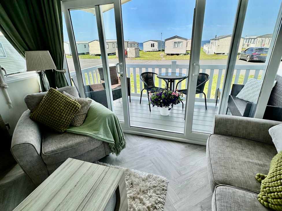 A living room with a sofa, coffee table and access to a balcony at Craig Tara Holiday Park 101 Bay View in Ayr