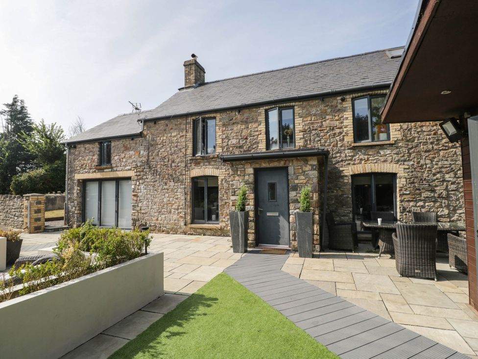 An outdoor view of a stone building with a patio and garden at Llanfarach Farmhouse near Pontyclun