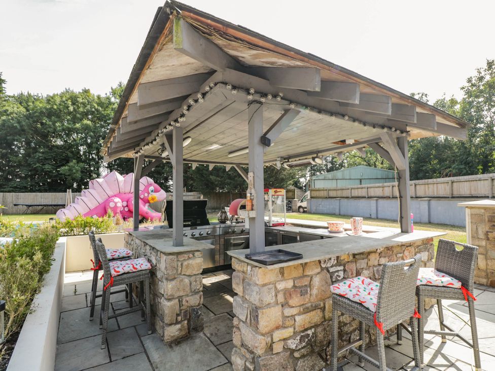An outdoor kitchen with a barbecue and bar stools at Llanfarach Farmhouse near Pontyclun