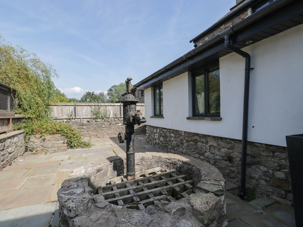 A garden with a stone well and patio area at Llanfarach Farmhouse near Pontyclun
