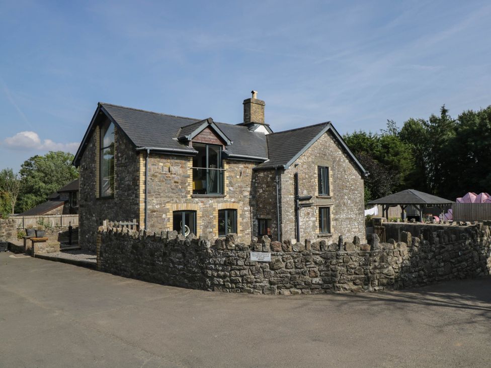 A stone house with a fence and parking area at Llanfarach Farmhouse near Pontyclun