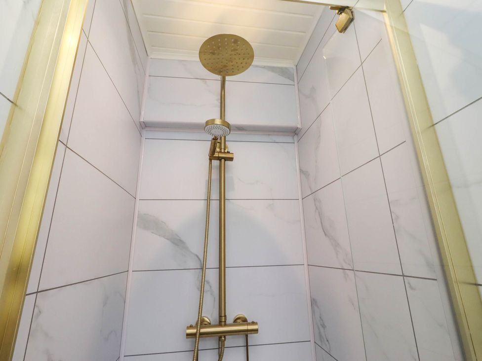 A shower with a gold showerhead and valve at Hedley Dene Cottage Longhorsley