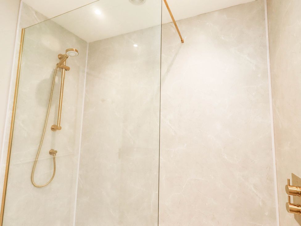 A shower with glass partition and gold fixtures at Hedley Dene Cottage Longhorsley