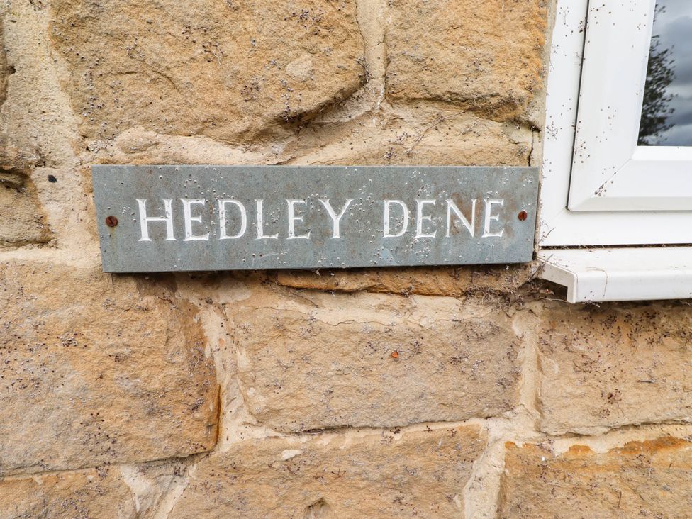 A sign displaying 'HEDLEY DENE' attached to a stone wall at Hedley Dene Cottage in Longhorsley