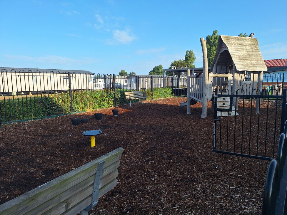 A playground with a wooden play structure and benches at Haven Seashore, Ellerton Willerby Xtra, Great Yarmouth