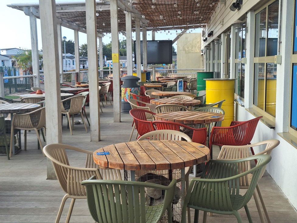 A restaurant patio with wooden tables and colorful chairs at Haven Seashore, Ellerton Willerby Xtra, Great Yarmouth