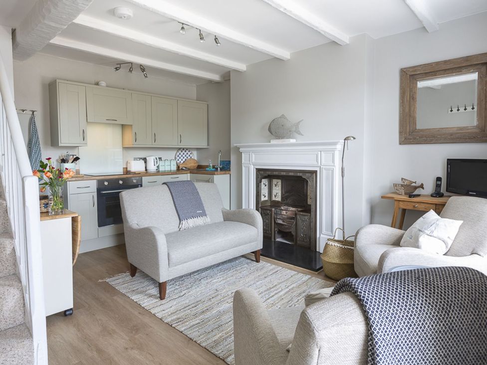 A living room with a fireplace and kitchen area at Primrose Cottage in Salcombe