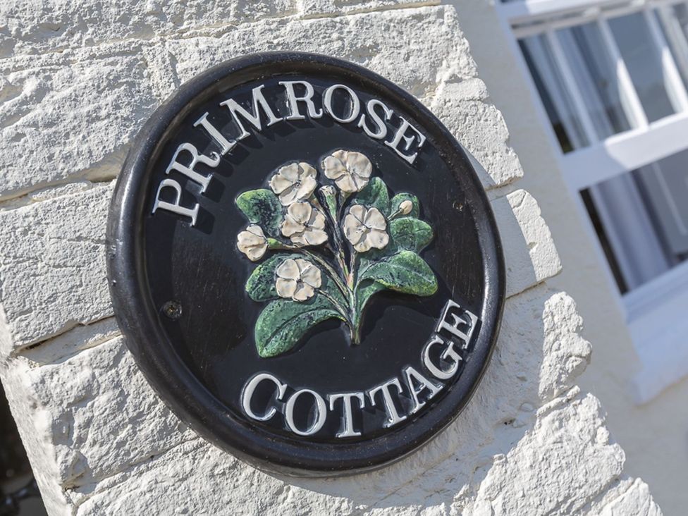 A sign for Primrose Cottage with flowers on it in Salcombe