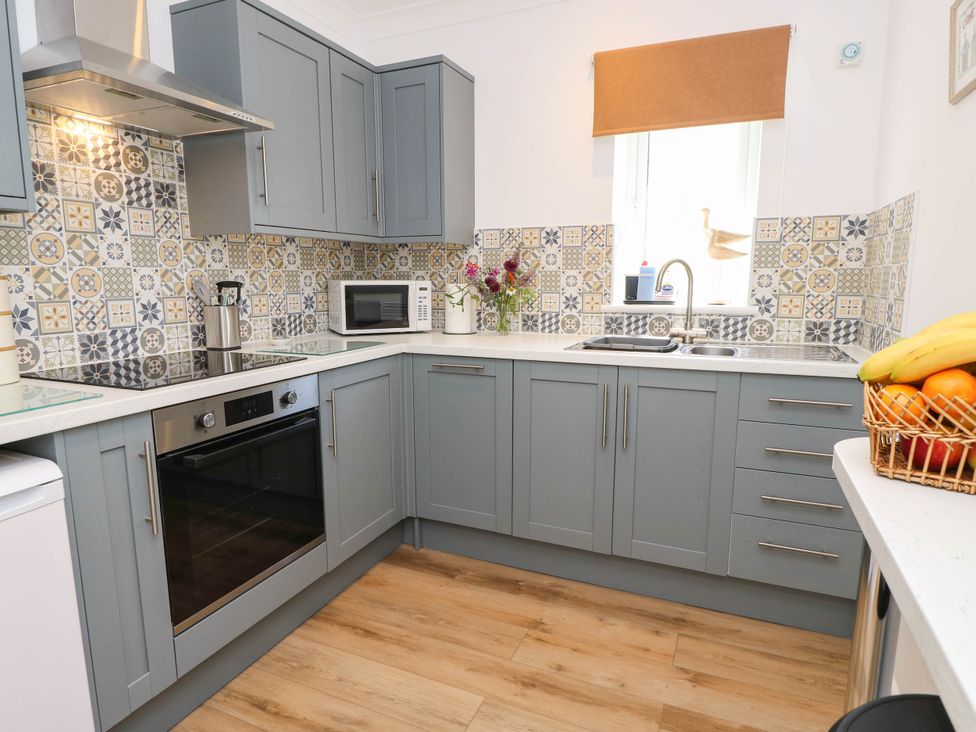 A kitchen with cabinets, stove, sink, and a basket of fruit at The Old Post Office St. Lawrence near Ventnor