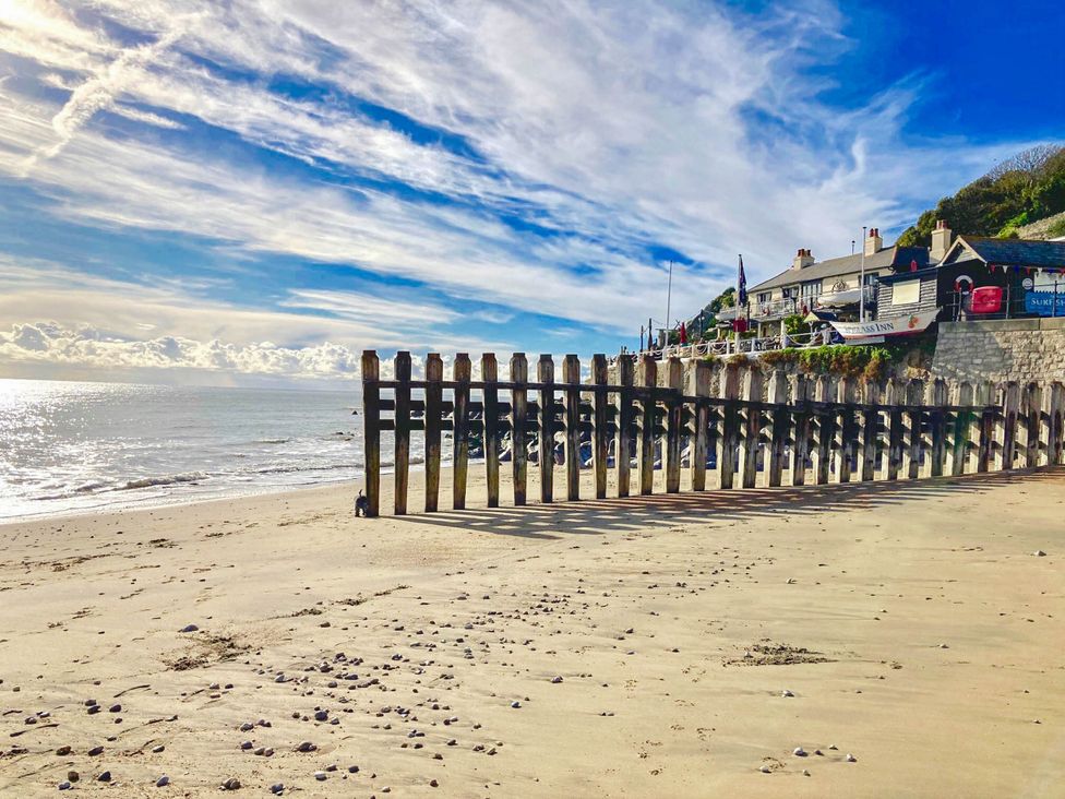 A beach with wooden posts and a restaurant in the background at The Old Post Office St. Lawrence near Ventnor