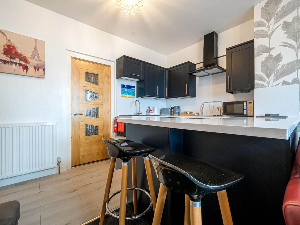 A kitchen with bar stools and black cabinets at Ground Floor 1Bed Apartment at SeaCote in Bispham