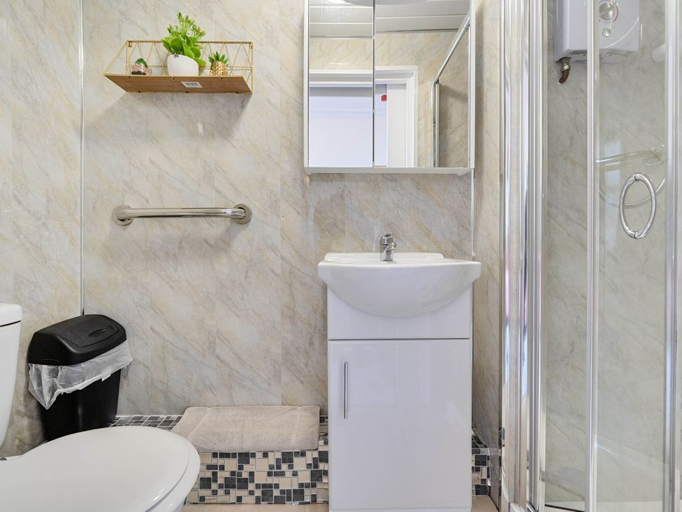 A bathroom with a sink, toilet, shower, and wall shelf at Ground Floor Studio Apartment at SeaCote, Bispham