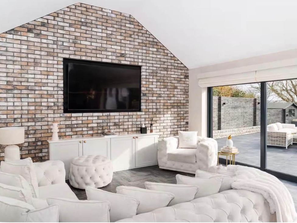 A living room with a television mounted on a brick wall at Rochester Retreat Spacious 5 Bedroom House in Higham