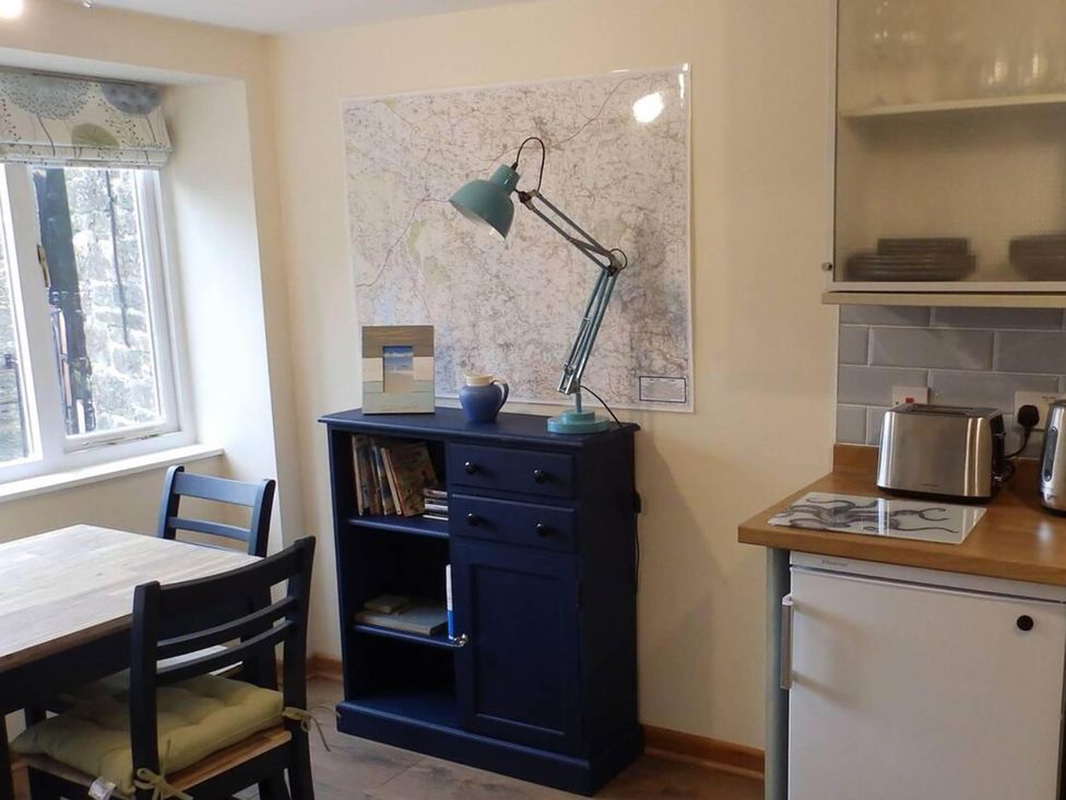 A kitchen with a table and bookshelf at 1 bed cottage Parking Patio close to coasts Coads Green near Launceston