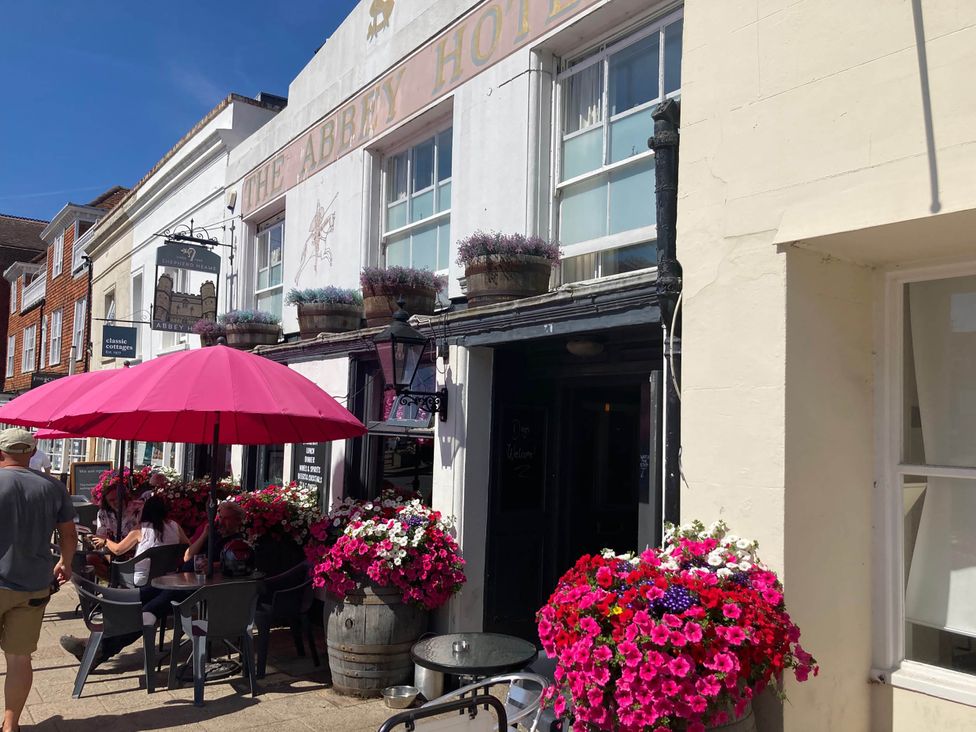 An outdoor seating area with flowers and a pink umbrella at The Abbey Hotel in Battle