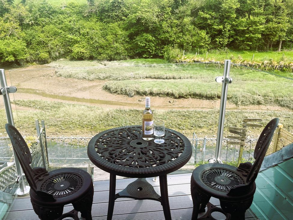 An outdoor table and chairs with a wine bottle and glass overlooking Little Petherick Creek in Little Petherick