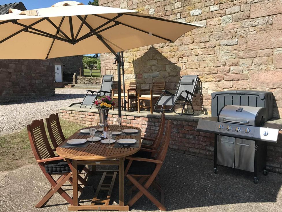 A dining area with a table, chairs, and grill at the outdoor space in Whiston near Cheadle