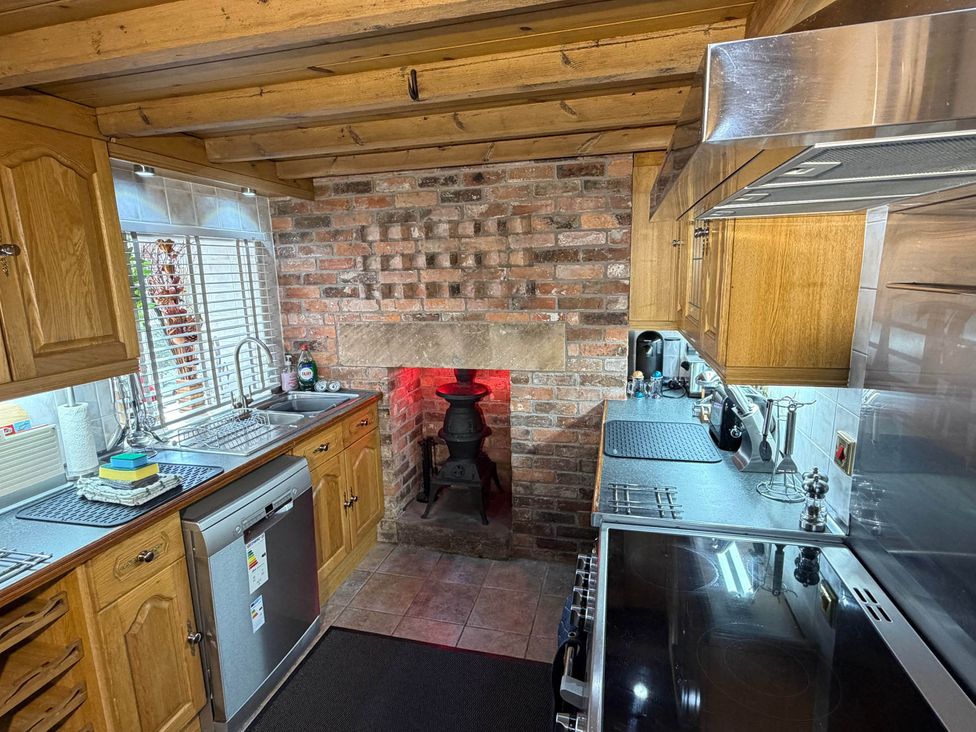 A kitchen with wooden cabinets and a brick fireplace at Farmhouse Sleeps 5 Near Alton Towers Peak District Cheadle