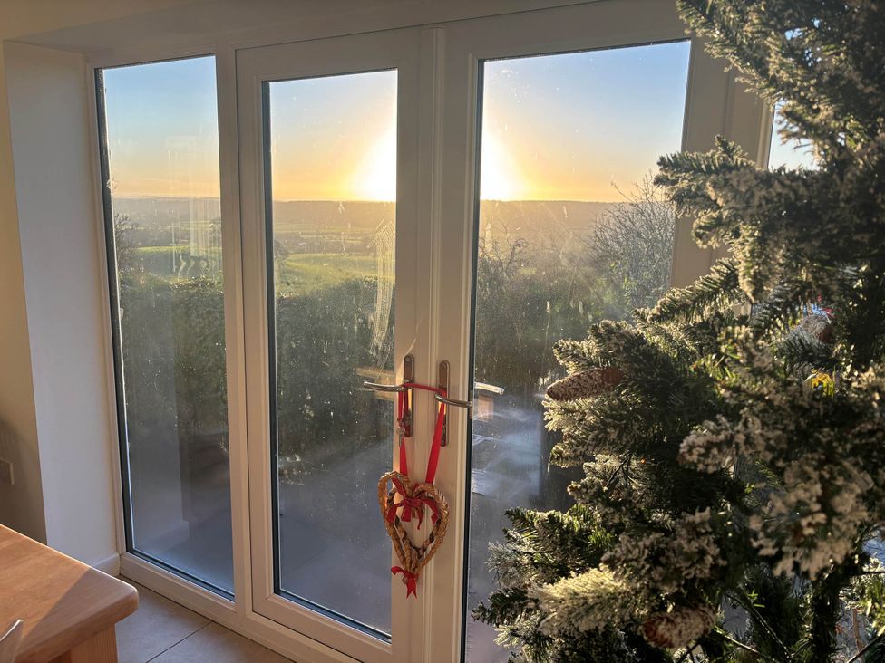 A view of a sunset through glass doors and a Christmas tree at Stunning 3 Bedroom Cottage near Historic York in Ampleforth