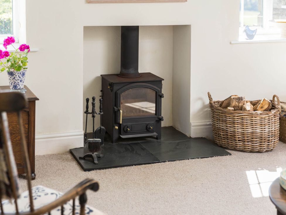 A living room with a wood stove and a basket of firewood at Stunning 3 Bedroom Cottage near Historic York in Ampleforth
