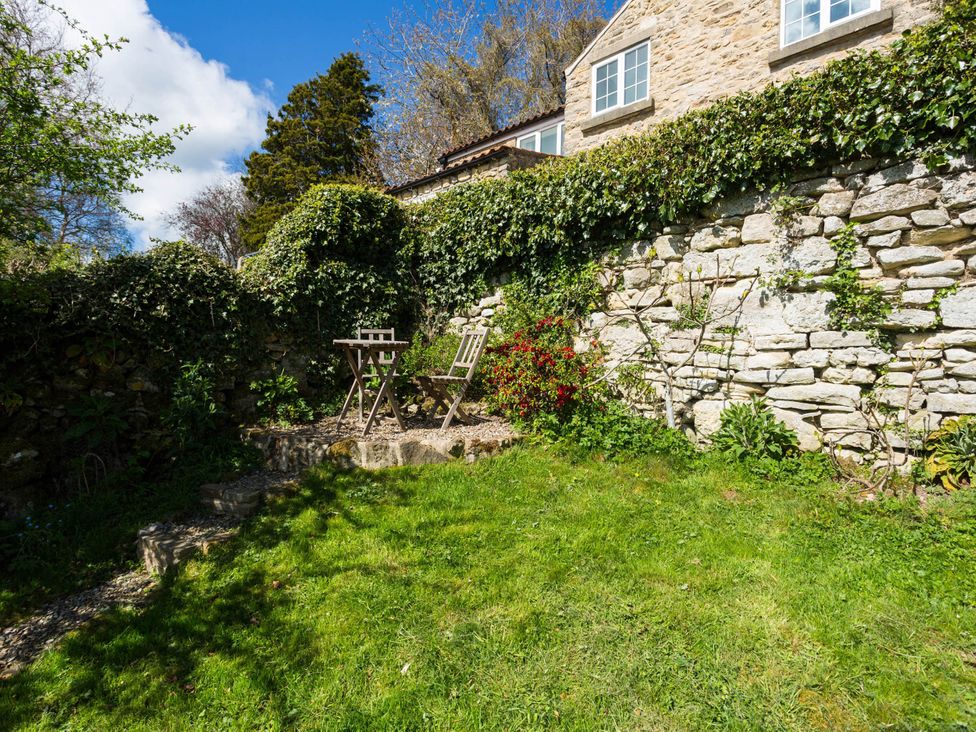 A garden with a table and chair near a stone wall at Stunning 3 Bedroom Cottage near Historic York in Ampleforth
