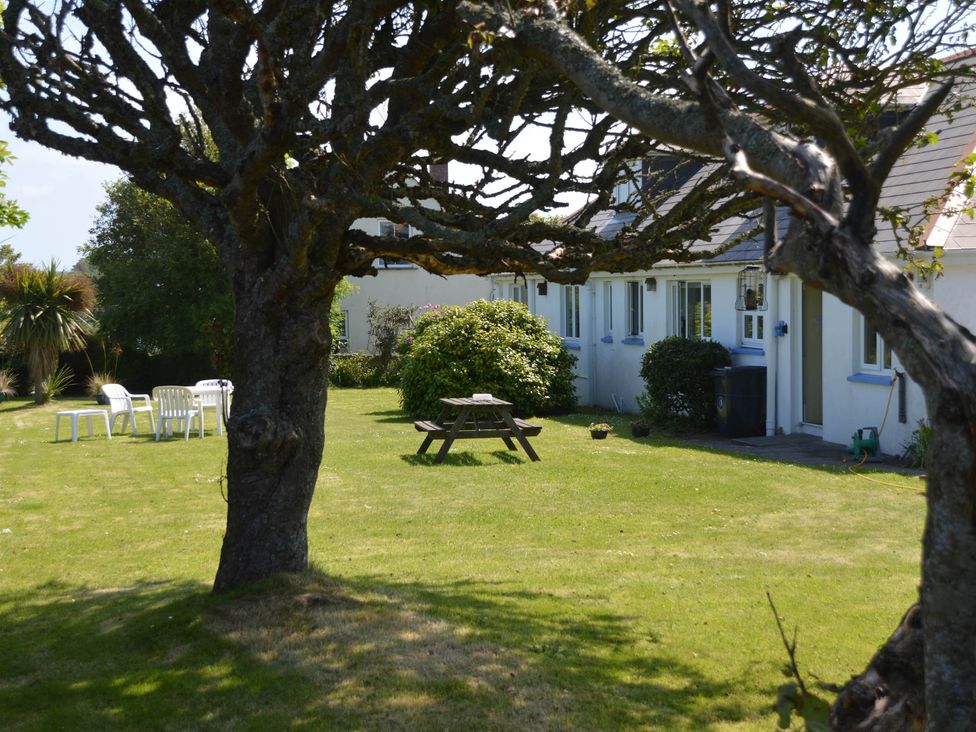 A garden with a tree, table, and chairs at House Sleeps 8 Close to Beach Free parking, Mullion