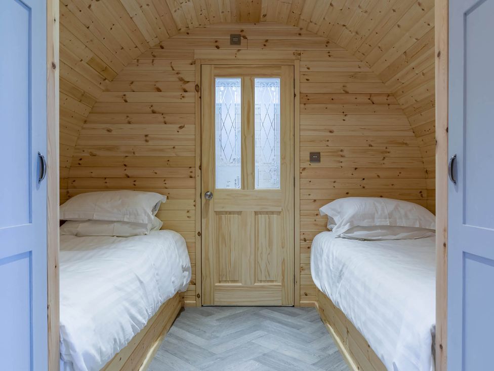 A bedroom with two beds and a wooden door at The Lodge at Brambles Farm Sleeps 4 Hot Tub in Leek
