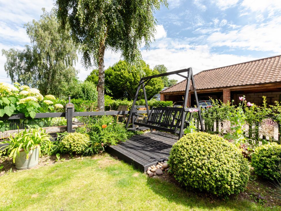 A garden with a swing bench and flower beds at 1880s Barn Conversion Sleeps4 Pet Friendly Hereford