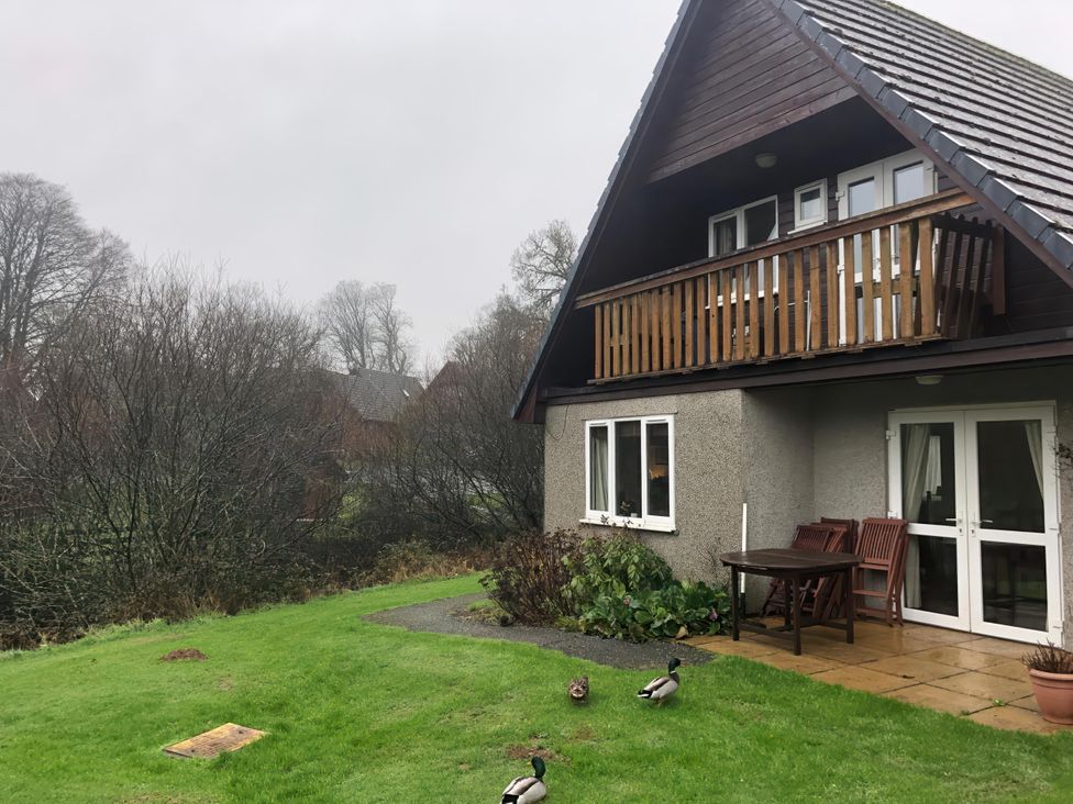 An outdoor view of a house with a balcony and table in the garden at Cosy 3 Bedroom House on Cornish estate with pool St Tudy