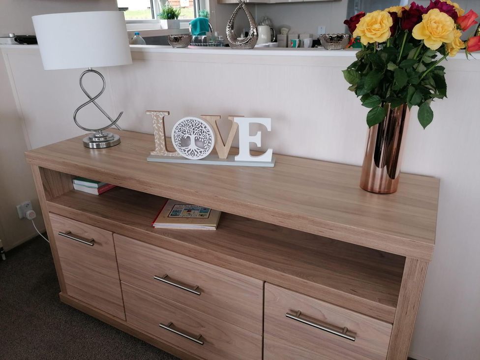A living room with a storage unit holding a lamp, flowers, and decorative items at Seaside Lodge Retreat in Eyemouth