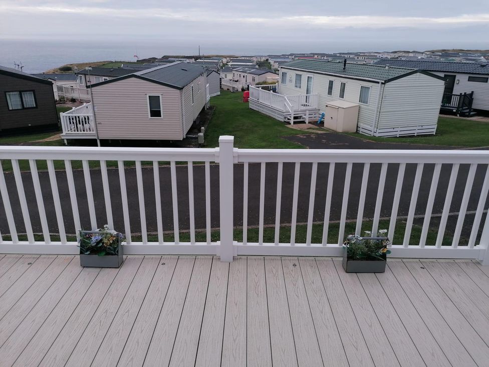 A deck with flowerpots overlooking caravans at Seaside Lodge Retreat in Eyemouth