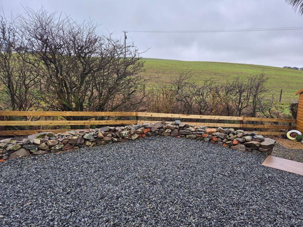 A garden with gravel, stone wall, trees, and a wooden shed at Beautiful 2Bed semi rural cottage enclosed garden in Stranraer