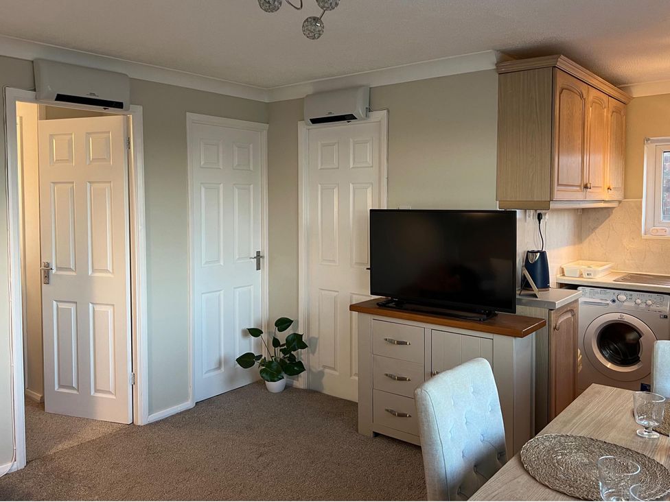 A living room with a television, dining table, and washing machine at The Old Barn in Manchester