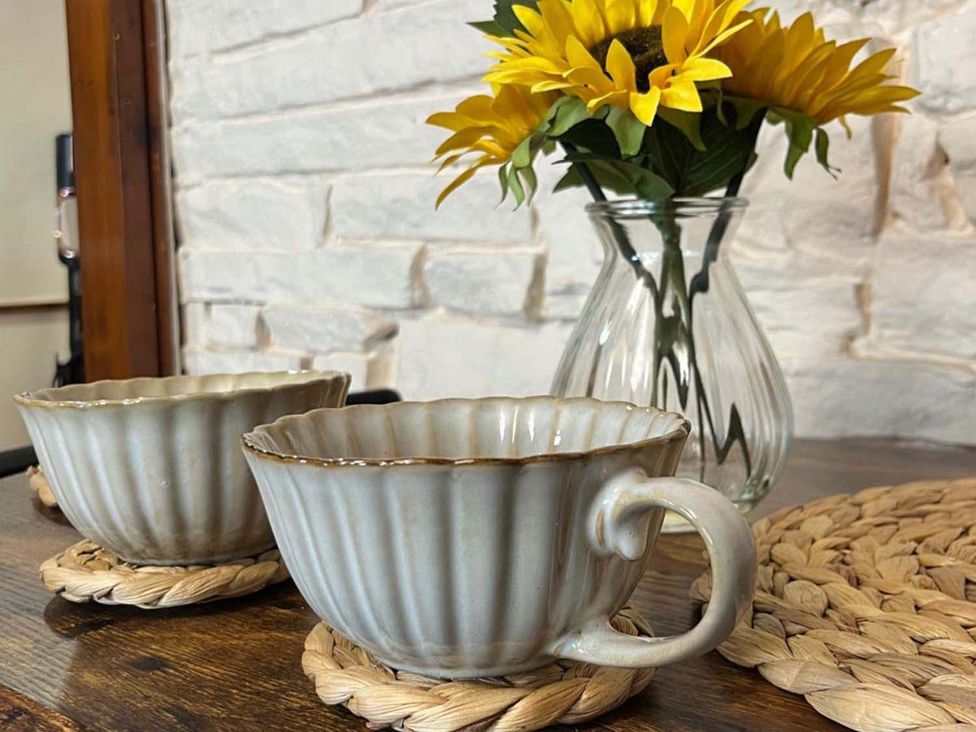 Two cups and a vase with flowers on a table at Cozy Cottage Retreat near Haworth log burner in Keighley