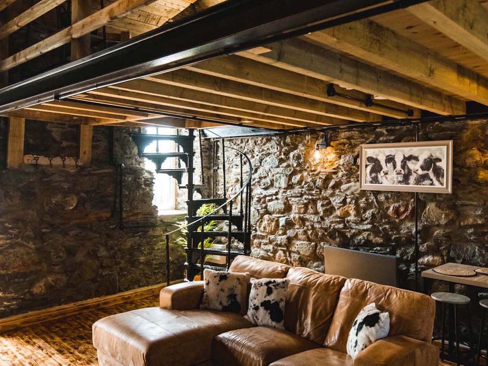 A living room with a sofa and spiral staircase at The Milking Shed at Pencraig Pet Friendly Llanynghenedl near Holyhead