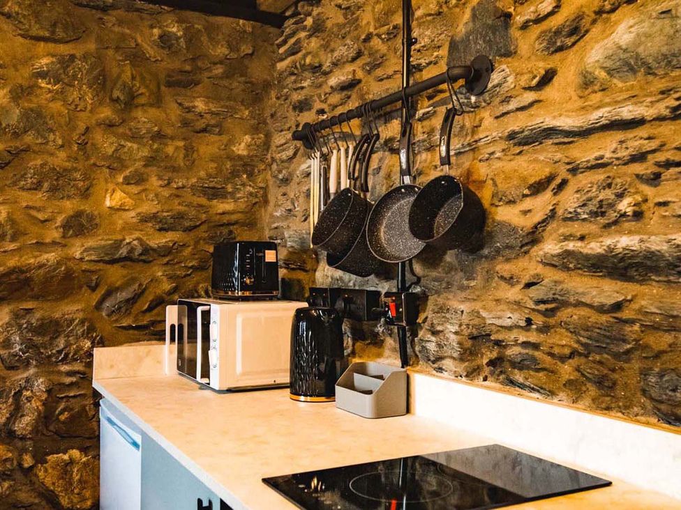 A kitchen with stone wall, microwave, kettle, and utensils at The Milking Shed at Pencraig Pet Friendly near Holyhead