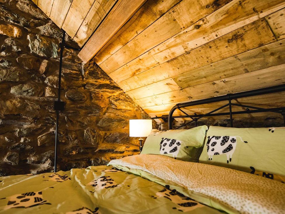 A bedroom with a bed and stone wall at The Milking Shed at Pencraig Pet Friendly near Holyhead