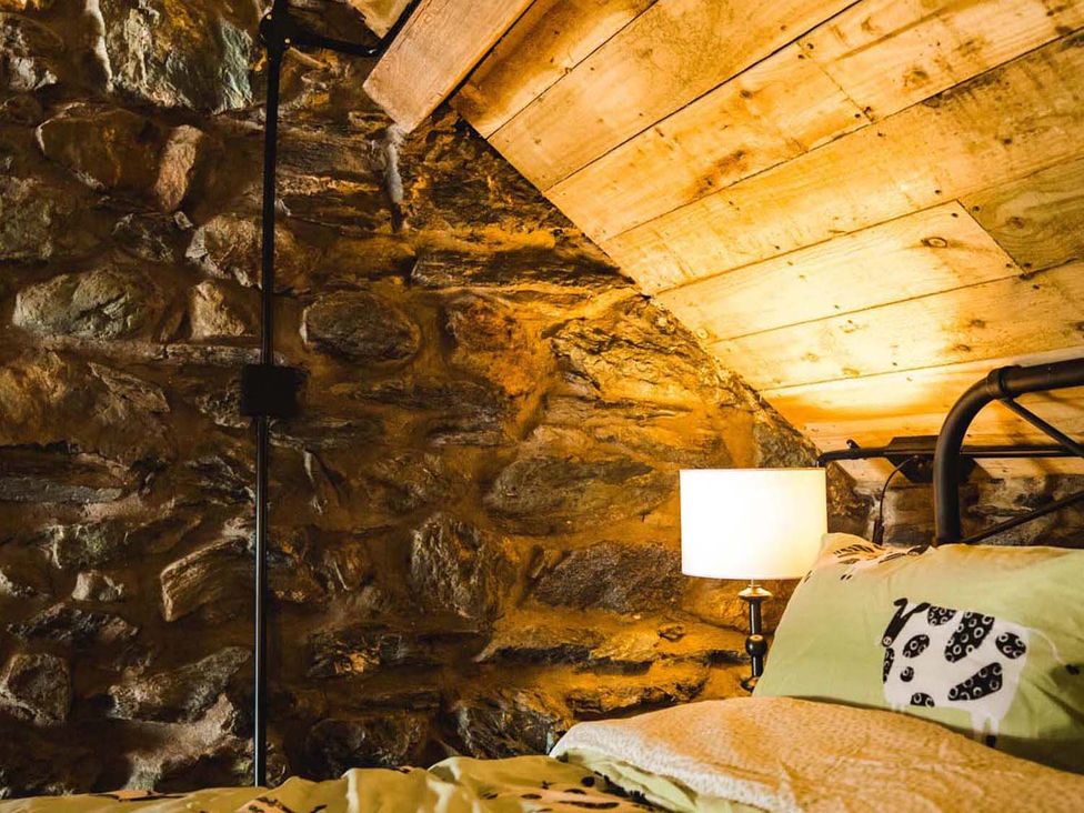 A bedroom with stone walls and wooden ceiling at The Milking Shed at Pencraig Pet Friendly near Holyhead