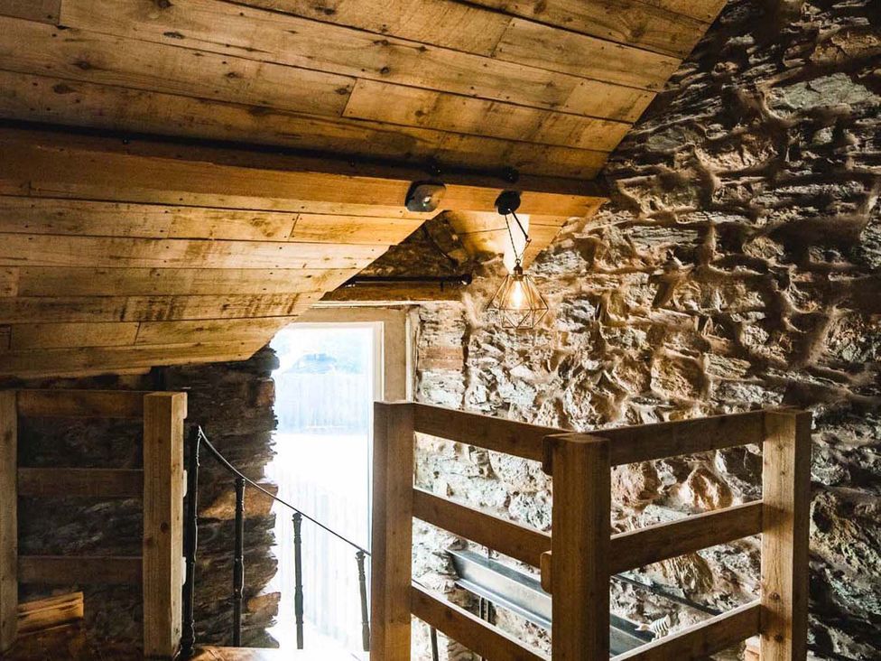 A loft area with wooden beams and stone wall at The Milking Shed at Pencraig Pet Friendly Llanynghenedl near Holyhead