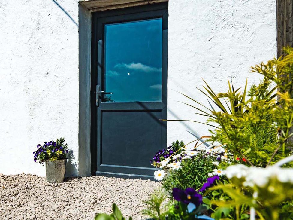 An entrance door with flowers in pots at The Milking Shed at Pencraig Pet Friendly near Holyhead